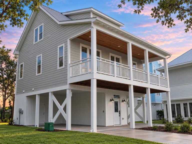 Front exterior of a Coastal Low Country style home featuring raised foundation, double front porches, horizontal siding, and open carport below