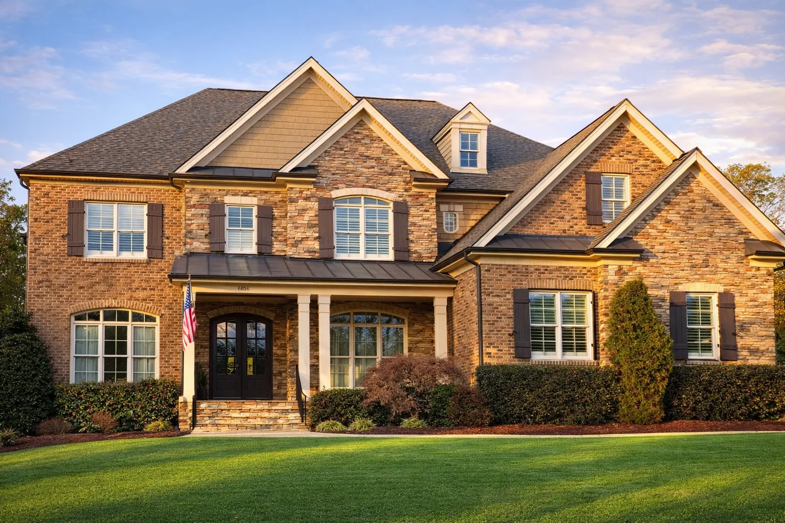 Front elevation of a Traditional Colonial New American home with brick exterior, stone detailing, symmetrical windows, and covered front porch