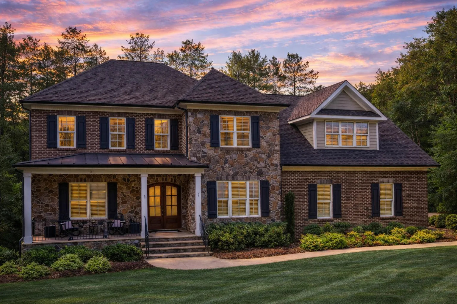 Front elevation of Traditional Colonial Revival home with brick and stone exterior, shutters, and covered front porch at sunset