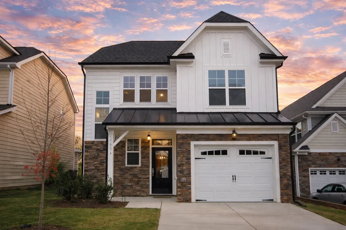 Front view of a Modern Farmhouse style home featuring board and batten siding, stone accents, and a one-car garage with dark wood doors.