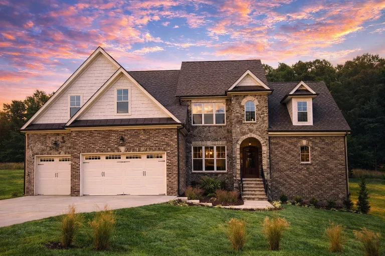 Front elevation of a French Country style home with stone exterior, steep shingle roof, arched entry, and symmetrical European-inspired design