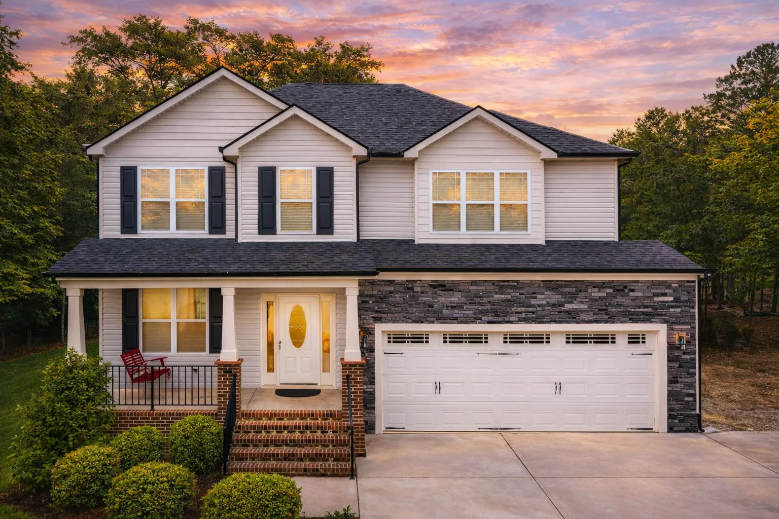 Front elevation of a Traditional Colonial home featuring beige horizontal siding, stone foundation accents, black shutters, and a welcoming covered porch entry.
