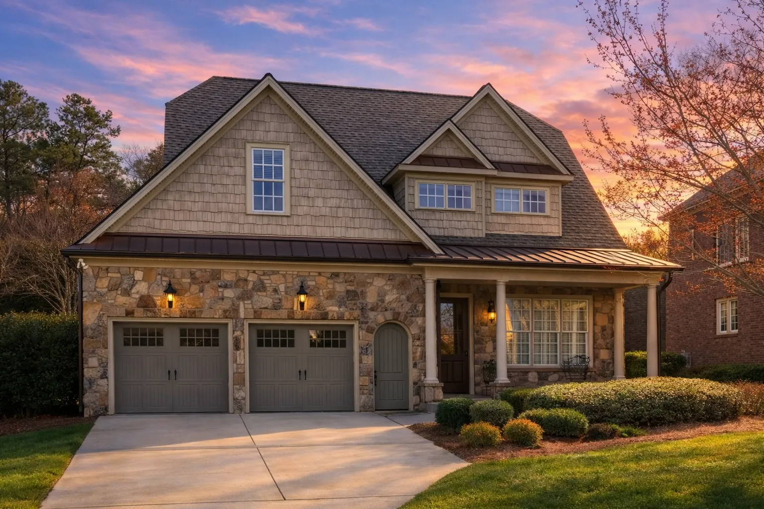 Front exterior view of a Shingle Style Traditional home with stone façade, cedar shake siding, gabled rooflines, and classic garage-forward design