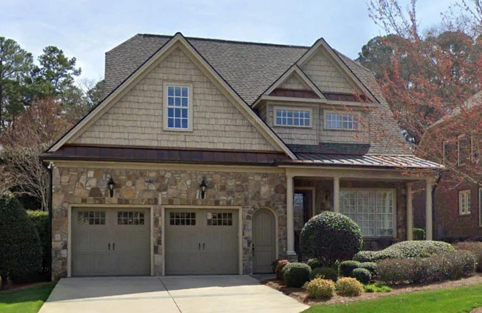Front exterior view of a Shingle Style Traditional home with stone façade, cedar shake siding, gabled rooflines, and classic garage-forward design
