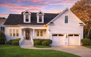 Front elevation of a modern farmhouse style home with horizontal siding, black garage doors, covered porch, and symmetrical rooflines
