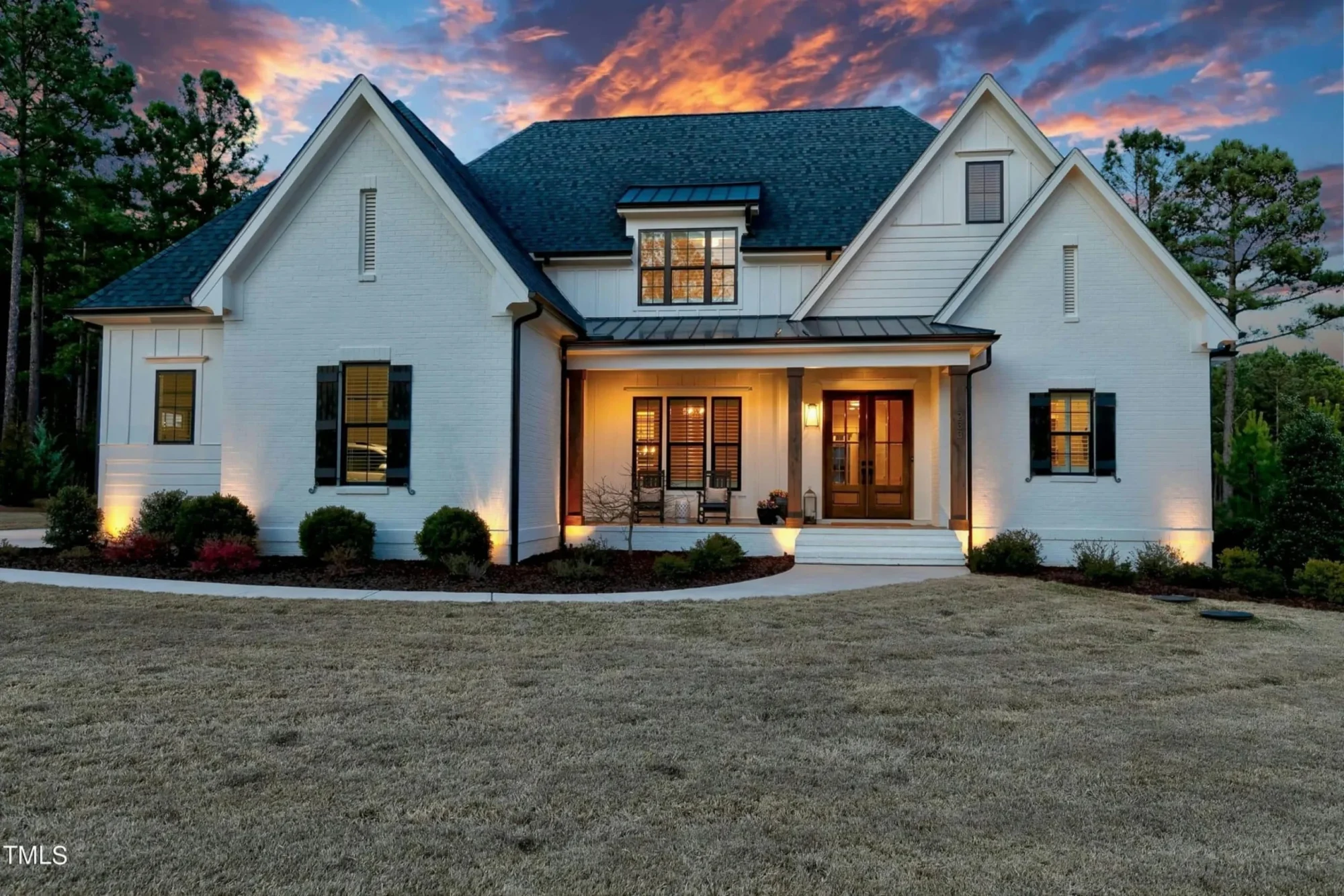 Front exterior view of a New American Modern Traditional house with painted brick, board and batten siding, symmetrical gables, and warm entry lighting