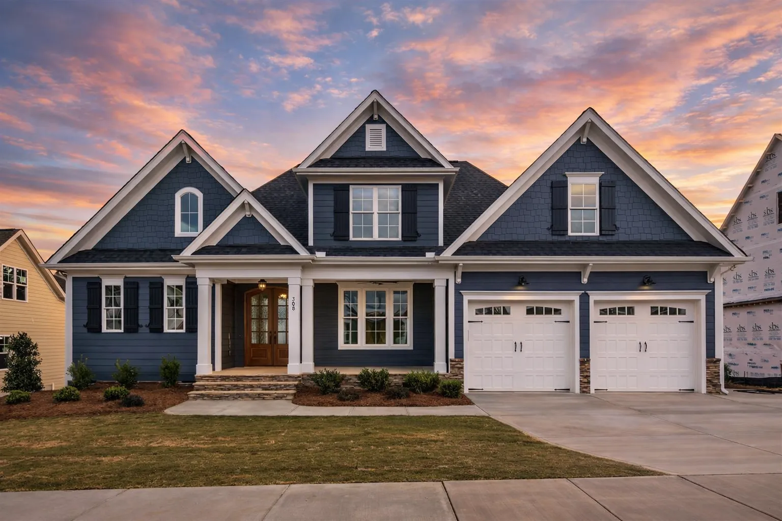 Front view of a Shingle Style Craftsman home with dark shingle siding, white trim, stone accents, and a two-car garage