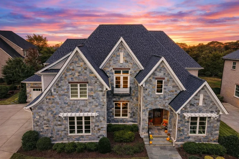Front exterior of a New American style home with full stone façade, steep gabled rooflines, French Country detailing, and manicured suburban landscaping
