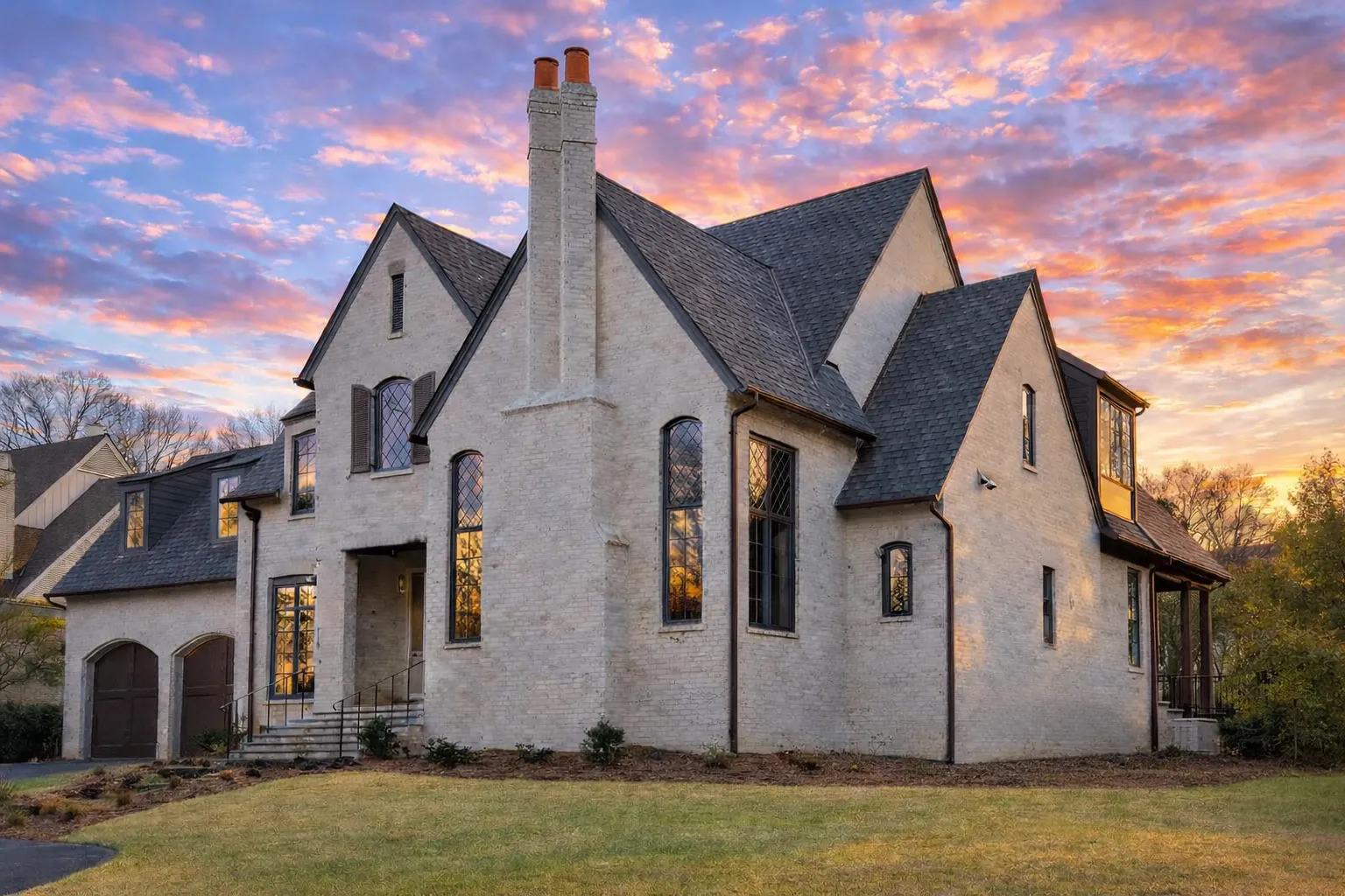Front view of Tudor Revival style brick home featuring steep gables, tall chimney, arched windows, and double wooden garage doors