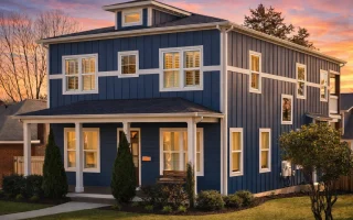 Front elevation of an American Foursquare style home featuring lap siding, board and batten accents, symmetrical windows, and a covered front porch