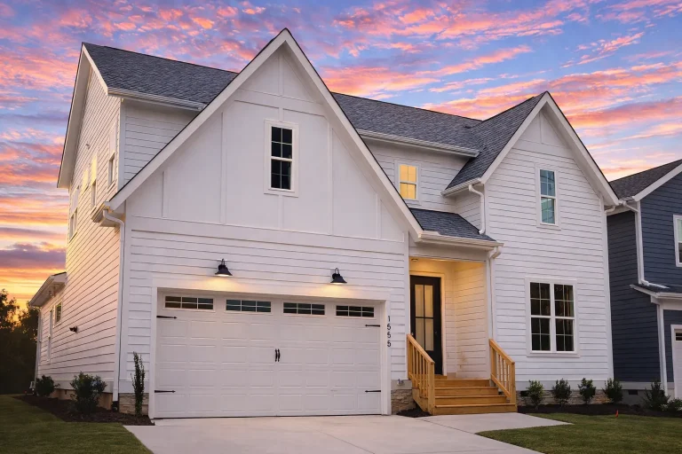Front elevation of a Modern Farmhouse home with white board and batten siding, gable rooflines, black windows, and a two-car front-entry garage