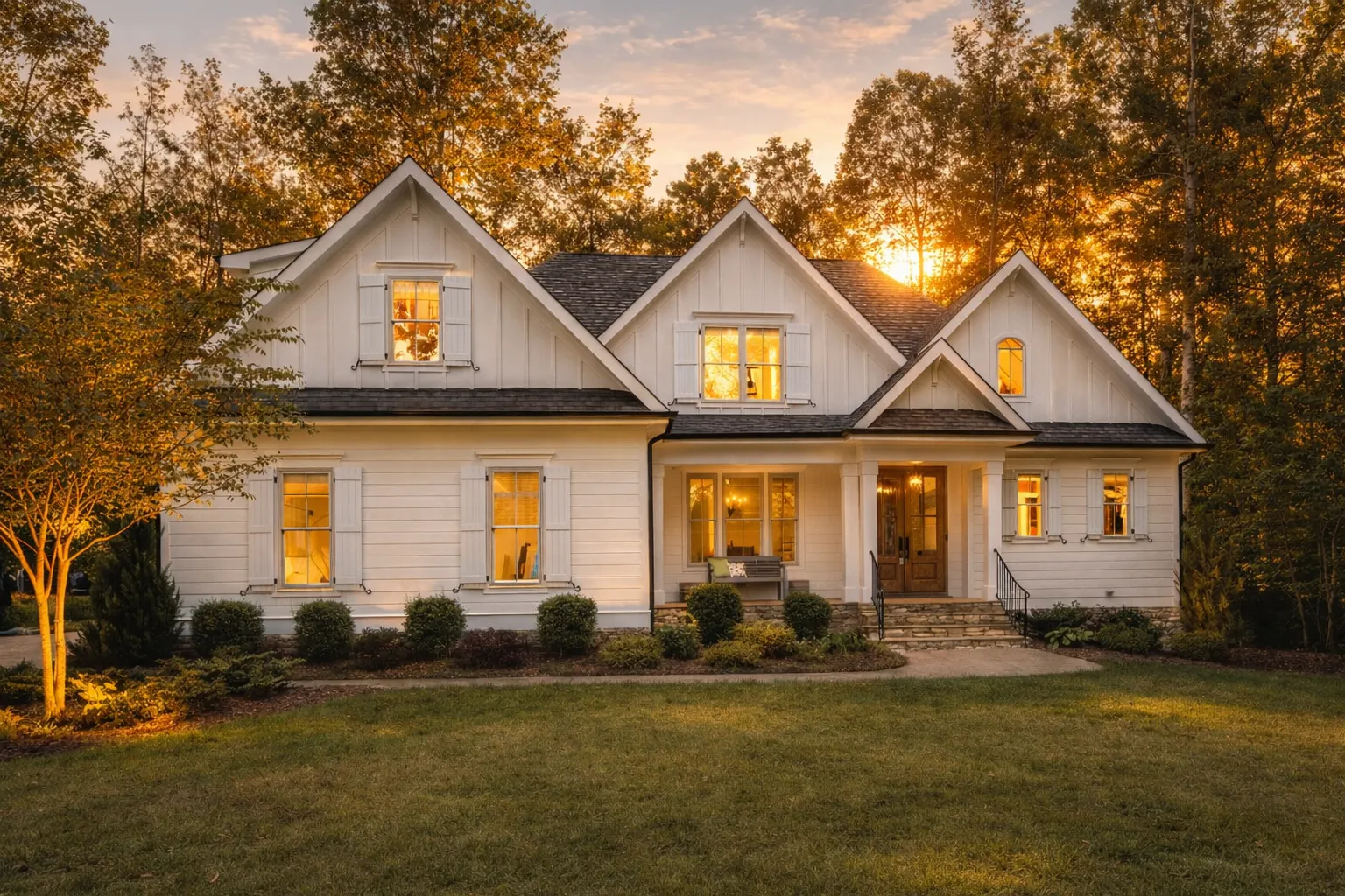 Front elevation of a Modern Farmhouse and New American style home with white horizontal siding, stone foundation accents, gabled rooflines, wood shutters, and a welcoming covered front porch