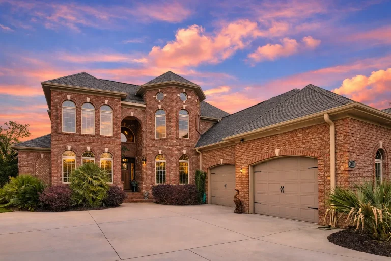 Front exterior view of a traditional brick Colonial home with Georgian symmetry, arched windows, and attached garage at sunset