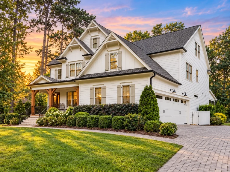 Front elevation of a modern farmhouse style home with board and batten siding, gabled rooflines, shutters, and a covered front porch surrounded by mature landscaping