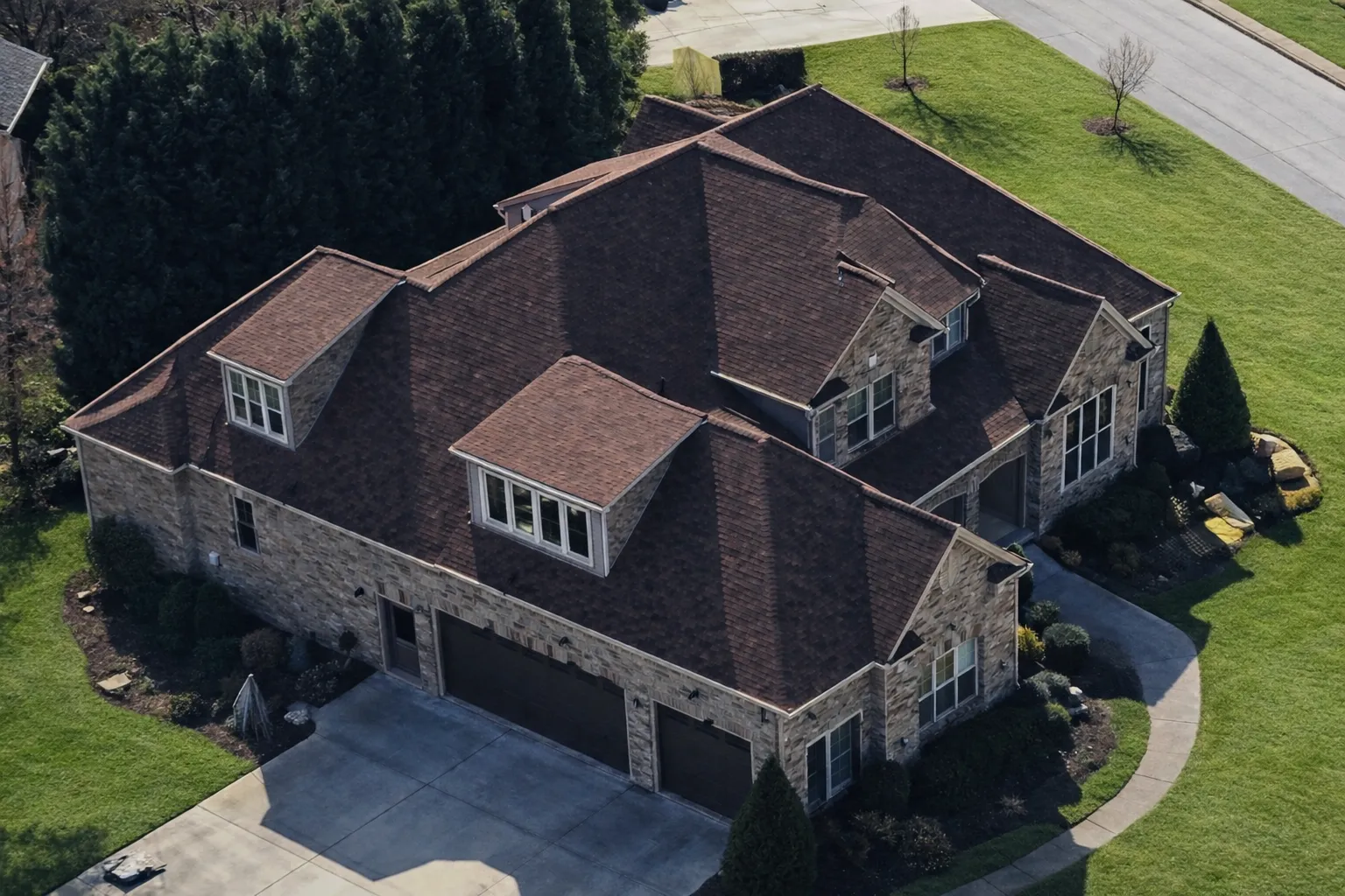 Aerial view of French Country style luxury home with brick exterior, steep hipped rooflines, dormer windows, and side-entry garage