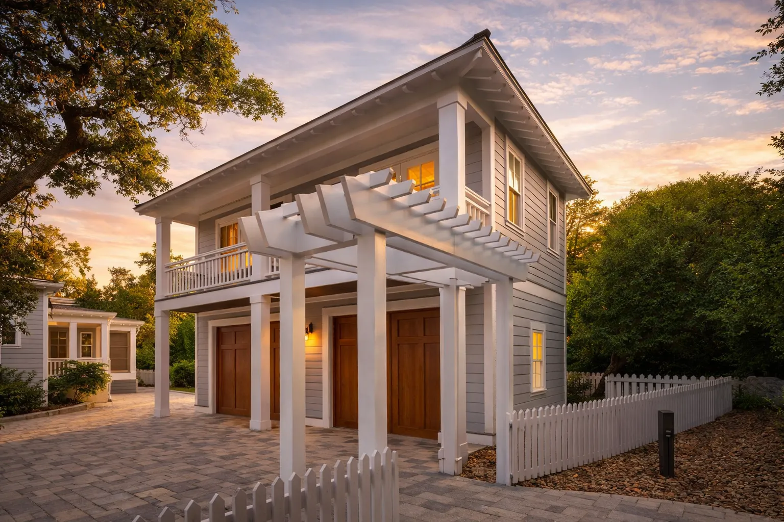 Front elevation of a coastal traditional carriage house with horizontal siding, upper balcony, and decorative pergola over a two-car garage
