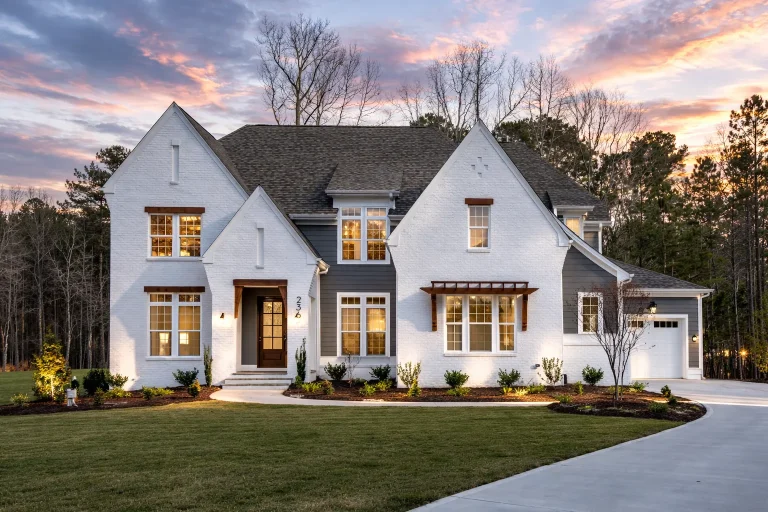 Front exterior of a New American Modern Farmhouse style home with painted brick, board and batten siding, steep gables, and a side-entry garage