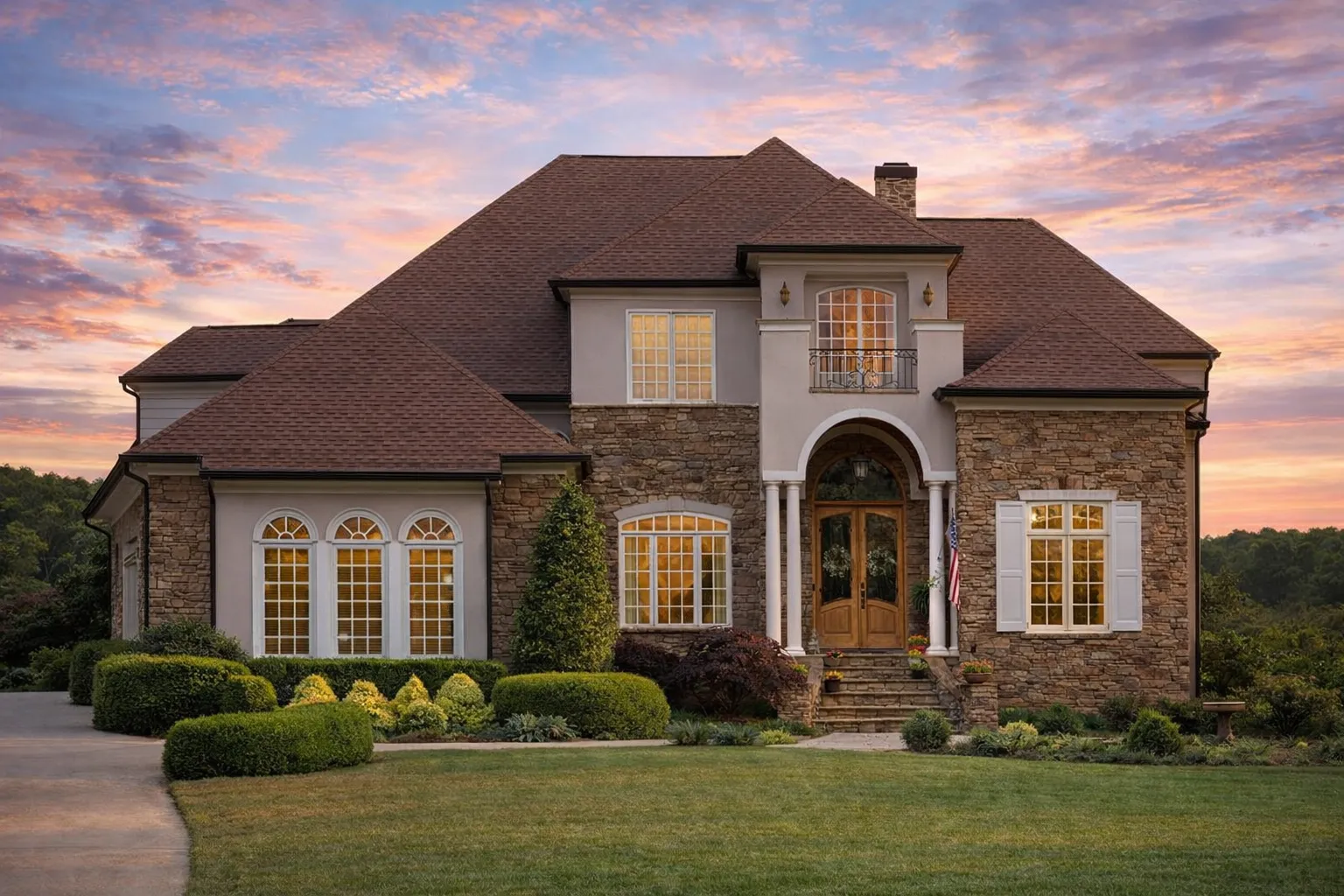Front elevation of a Neoclassical Traditional style home with stone and stucco exterior, arched entry, symmetrical windows, and classic columns