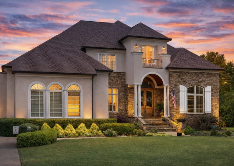 Front elevation of a Neoclassical Traditional style home with stone and stucco exterior, arched entry, symmetrical windows, and classic columns