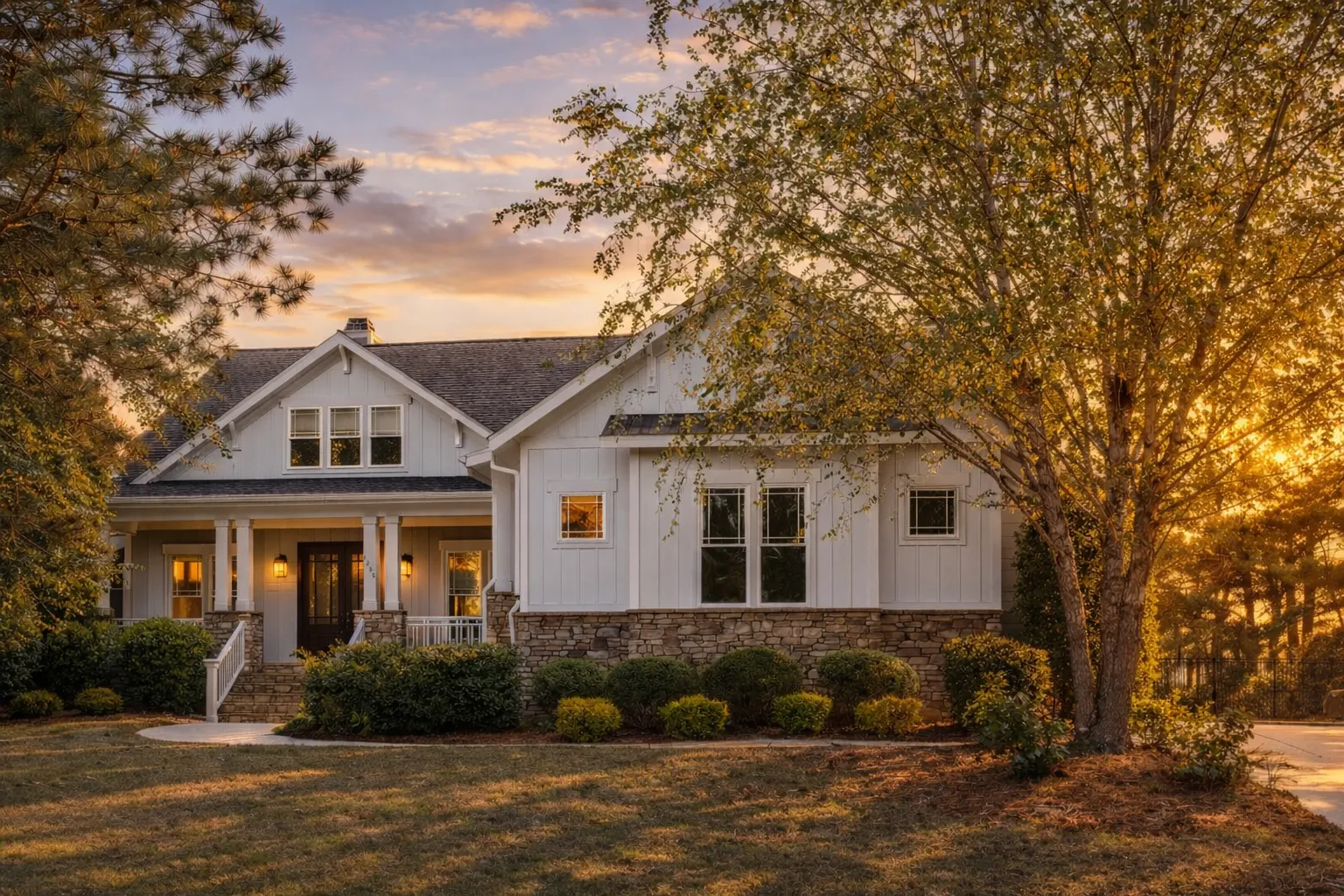 Front elevation of a Modern Farmhouse style home featuring white board and batten siding, stone base accents, gabled rooflines, and a welcoming covered porch