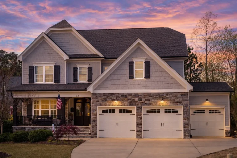 Front elevation of a New American Traditional house featuring horizontal siding, shingle accents, stone base, and a three-car garage