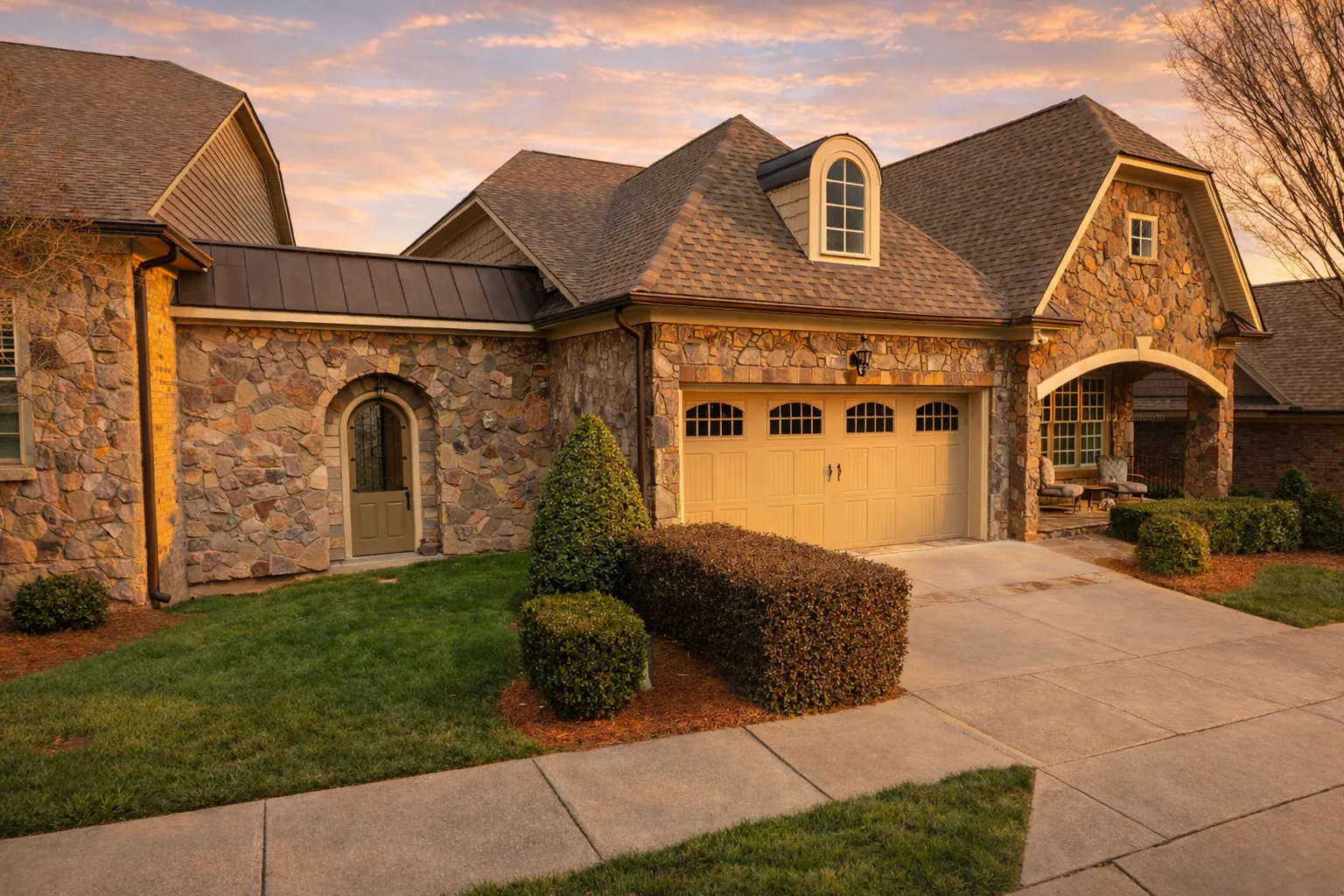 Front exterior of a French Country style home featuring natural stone façade, arched entryway, and traditional pitched rooflines
