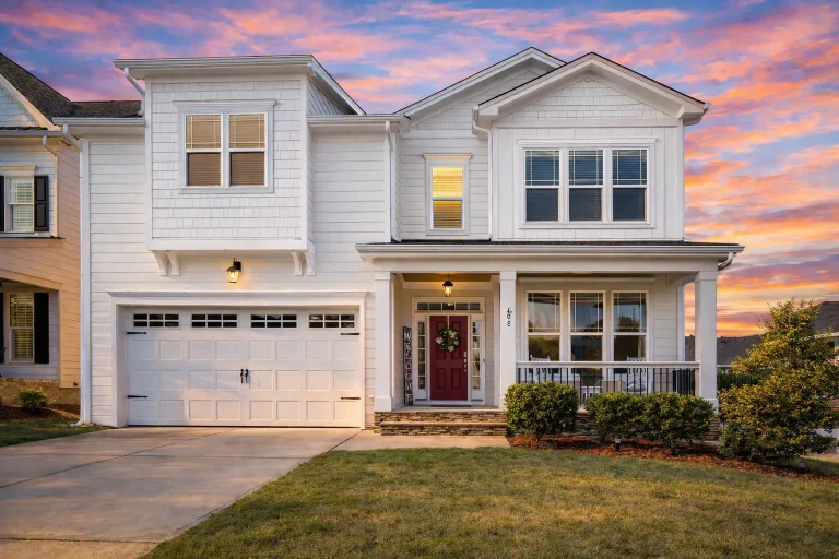 Front elevation of traditional suburban house with white horizontal siding, gabled rooflines, red front door, and covered porch
