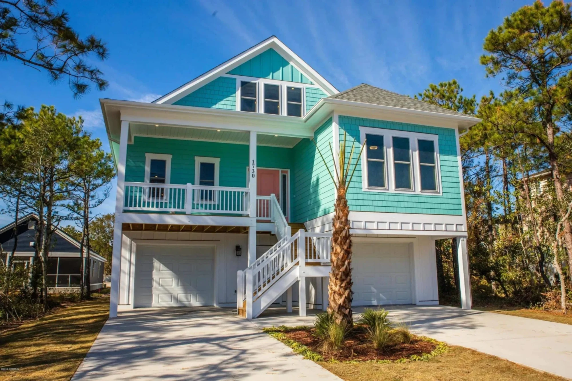Front exterior of an elevated Coastal Beach House with horizontal siding, covered porches, exterior stairs, and ground-level garage