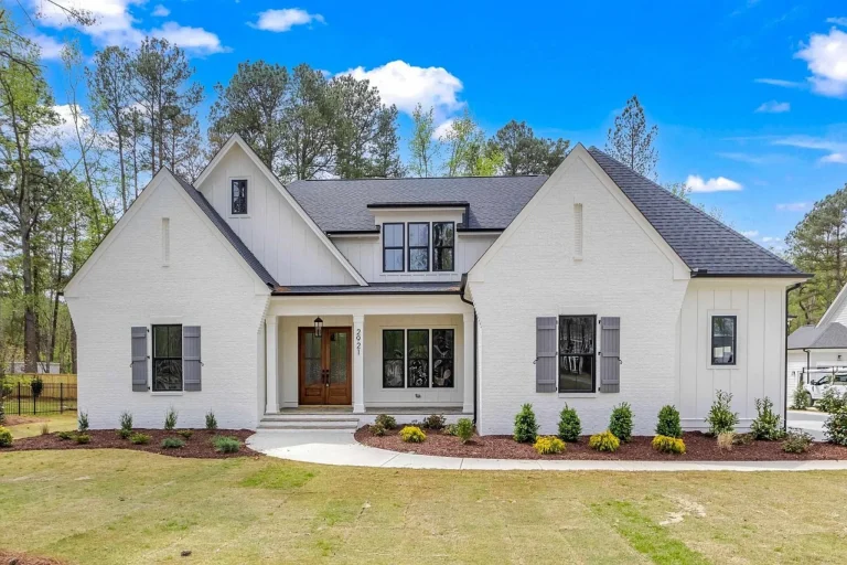 Front elevation of a Modern Farmhouse style home featuring white painted brick exterior, steep gable rooflines, black shutters, and welcoming covered entry