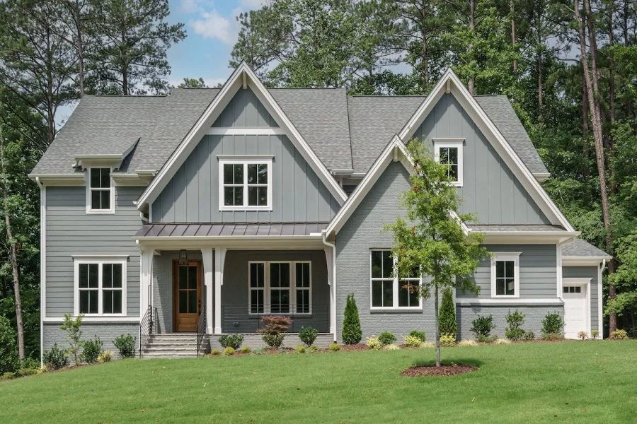 Front exterior of a New American modern traditional home with Colonial Revival influence, gray lap siding, board and batten accents, gabled rooflines, and covered front porch
