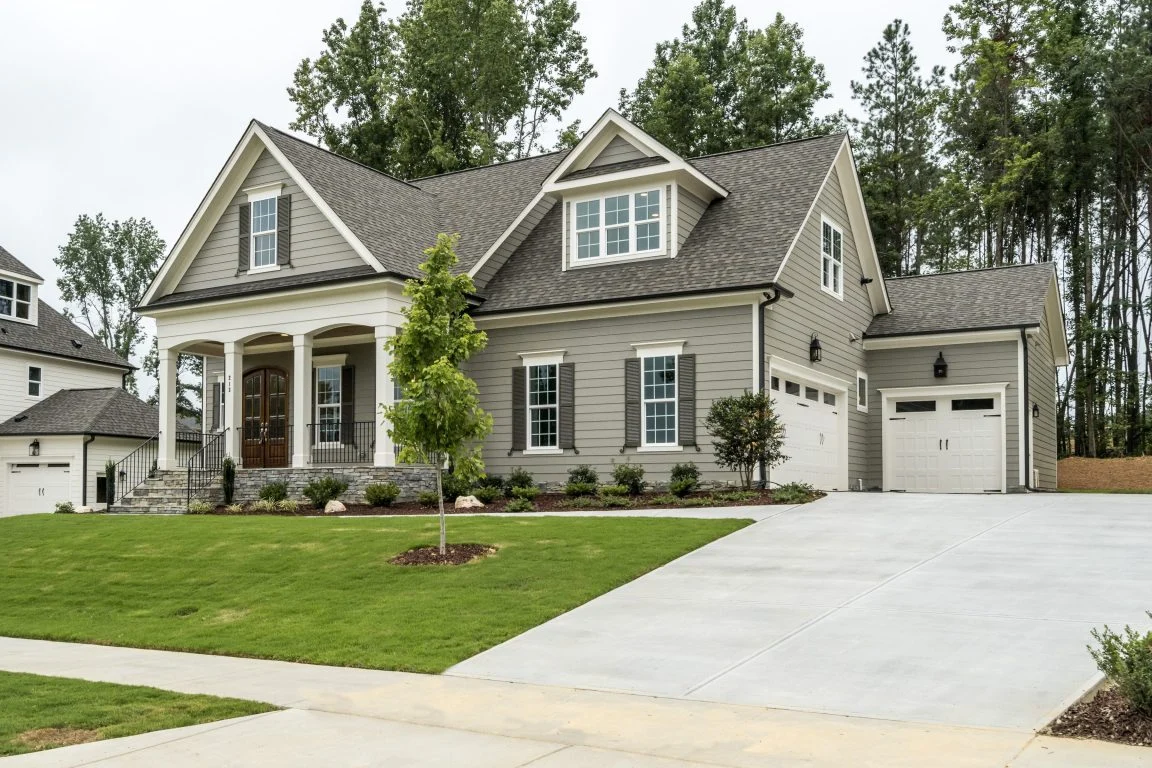 Front exterior of a New American Traditional style home with horizontal siding, board and batten accents, stone porch columns, gabled rooflines, and attached garage