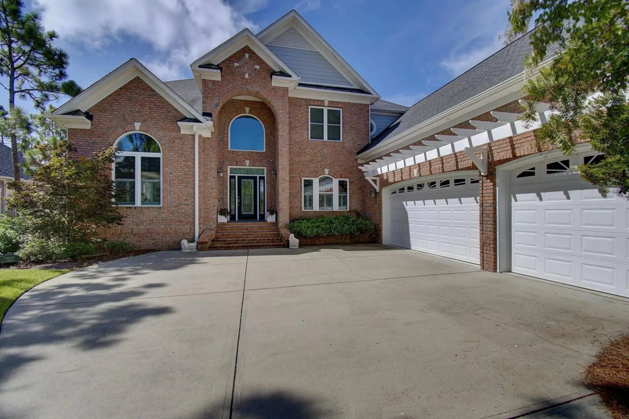 Front exterior view of a Traditional Colonial style brick home with symmetrical windows, arched entryway, and attached garage