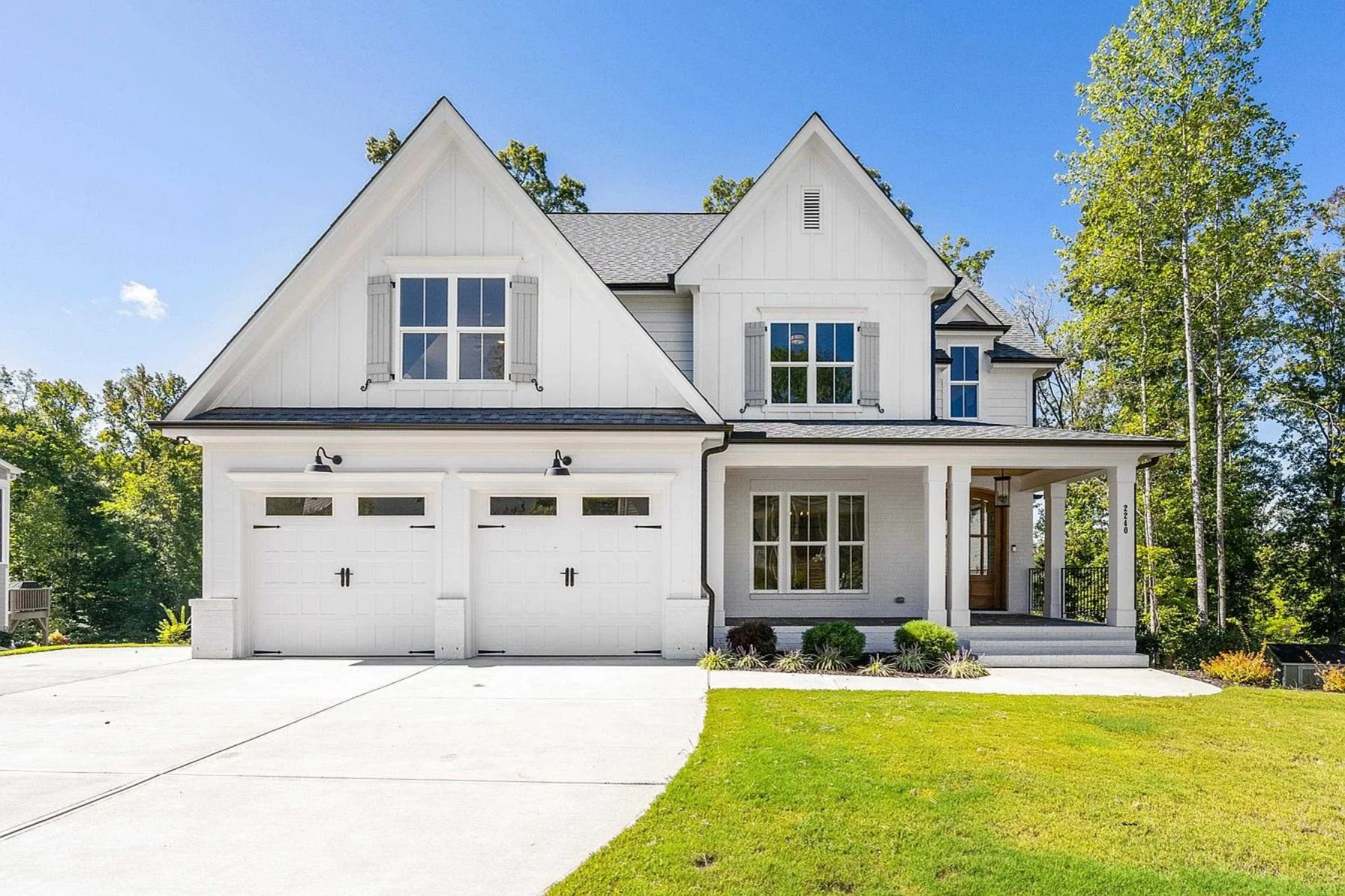 Front exterior view of a New American Modern Traditional farmhouse home with white board and batten siding, steep gables, covered porch, and attached garage