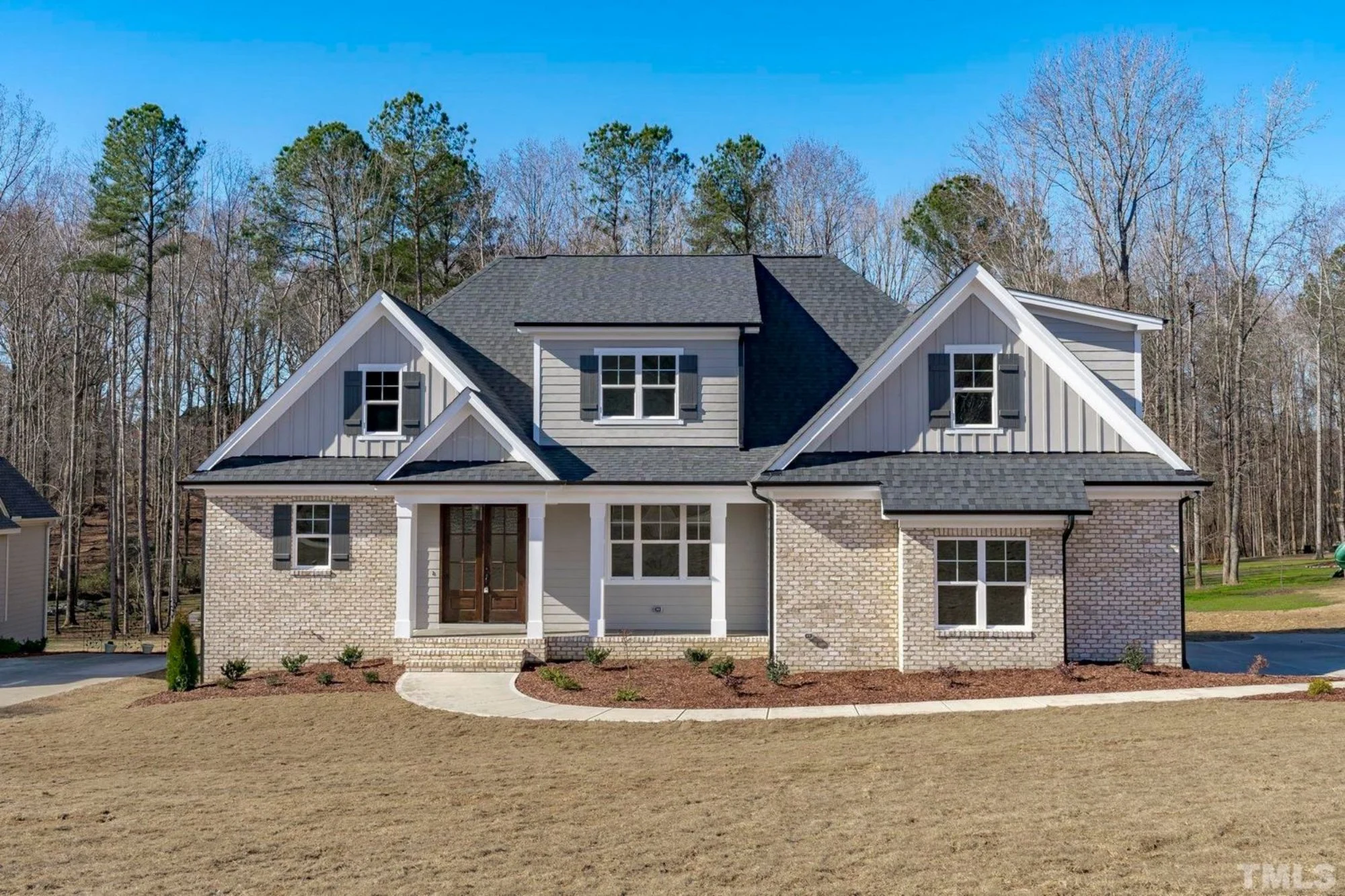 Front elevation of a New American style home with brick exterior, board and batten gables, symmetrical rooflines, and traditional suburban curb appeal