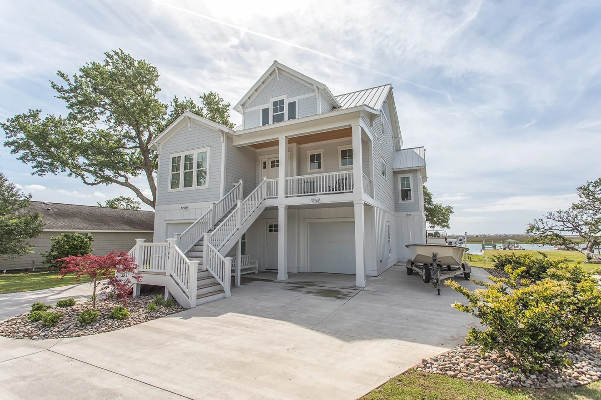 Front elevation of an elevated Coastal Low Country style home featuring lap siding, board and batten accents, covered porches, exterior stairs, and a standing seam metal roof