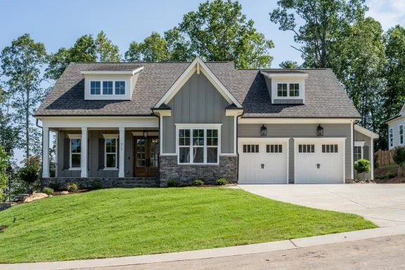 Front elevation of a Modern Farmhouse style home featuring board and batten siding, stone accents, gabled rooflines, and a covered front porch
