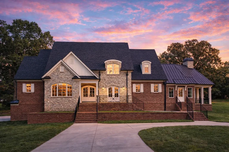 Front elevation of French Country style home with brick and stone exterior, arched doorway, dormer windows, and side-entry garage
