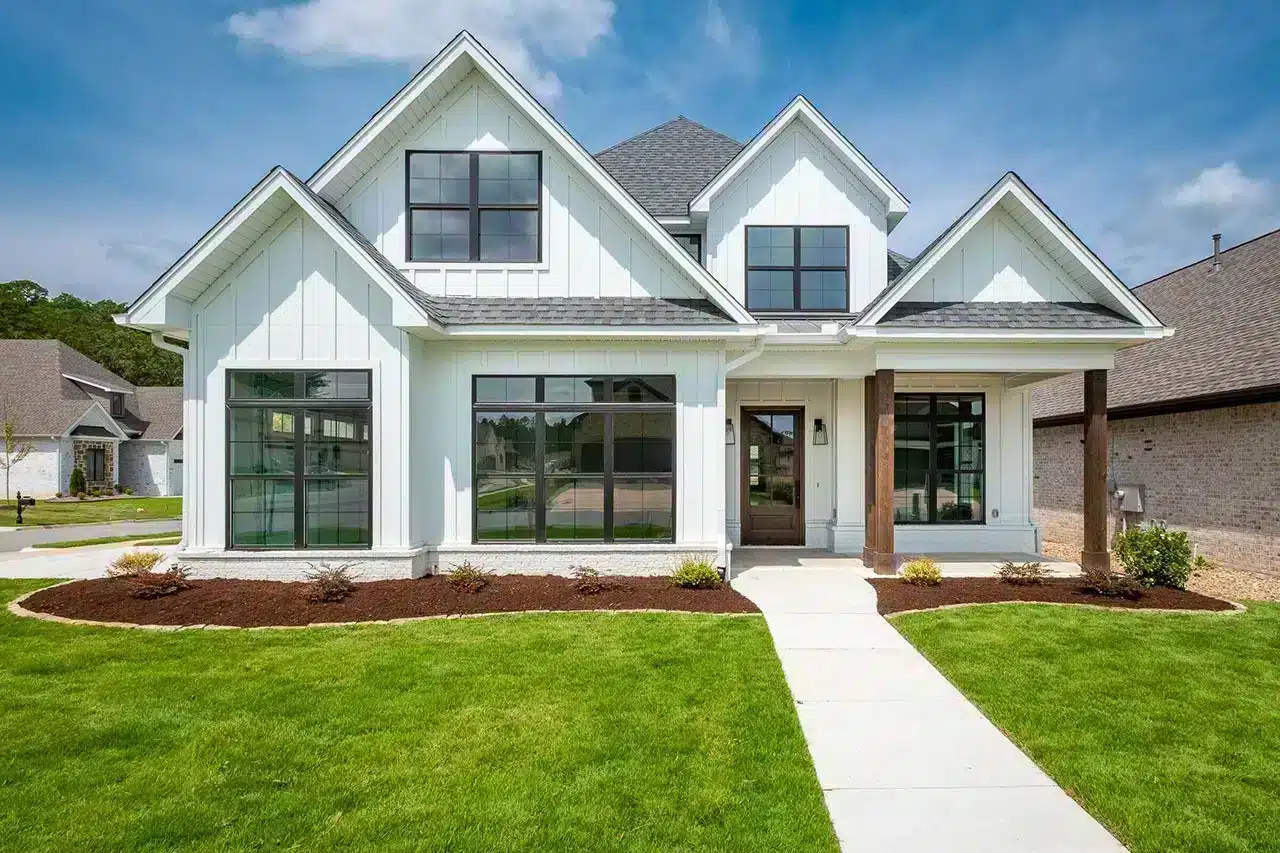 A modern two-story, 3 bedroom house plan with white siding, large windows, and a covered front entrance, surrounded by a green lawn and fresh landscaping under a blue sky—perfect for your house Plan Wishlist.