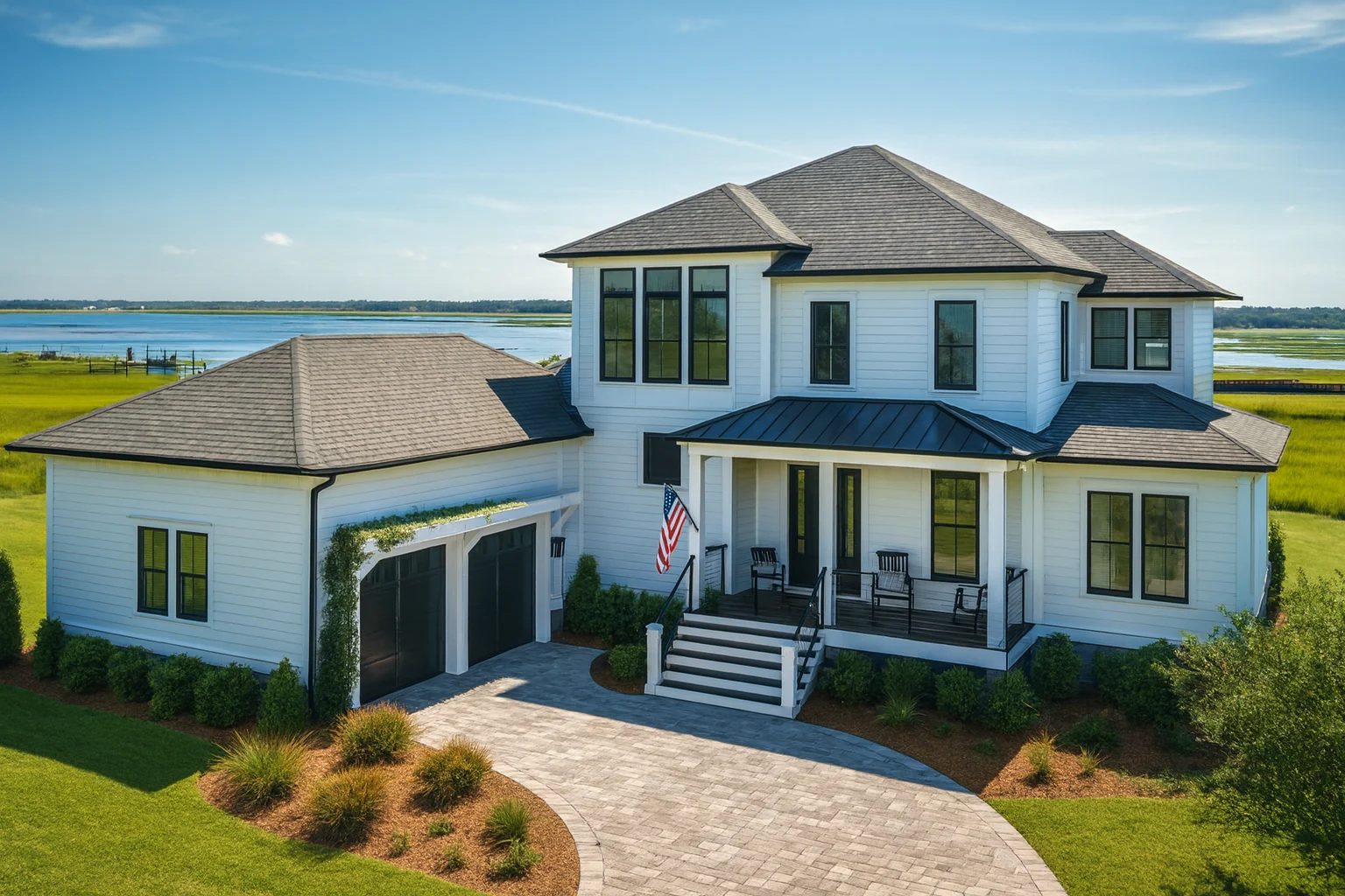 Front exterior of a modern coastal farmhouse with white siding, black windows, standing seam metal roof, and expansive covered porch