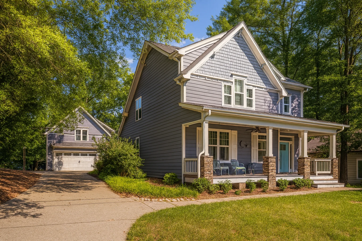 Front exterior of a New American Craftsman style home with lap siding, shingle accents, covered porch, and detached garage